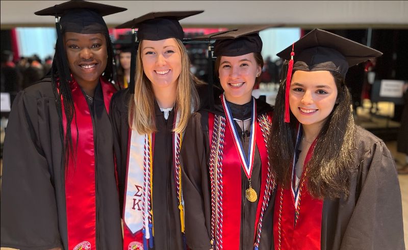 four students in graduation attire with red sashes and french honor cords 2022