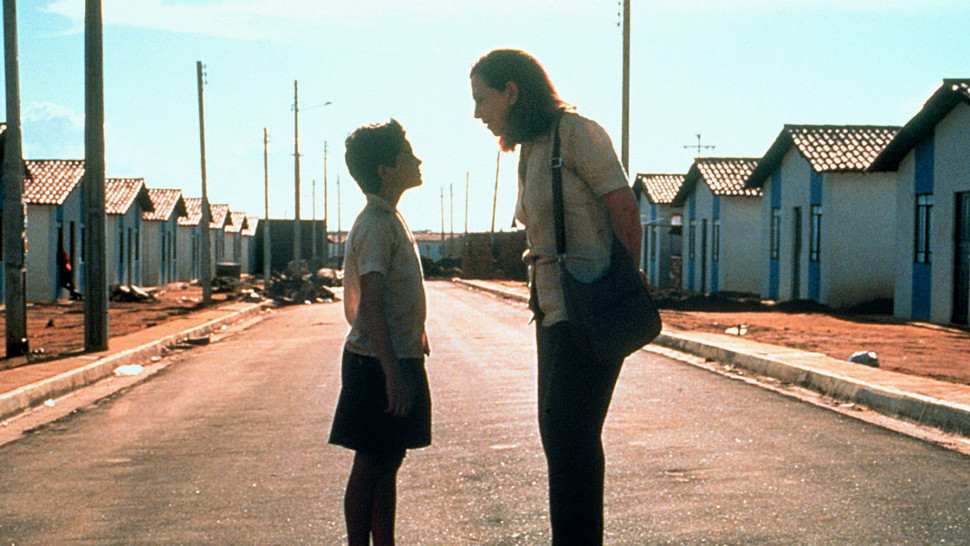 still image from central station film, a woman stands over a young boy with small houses in the background